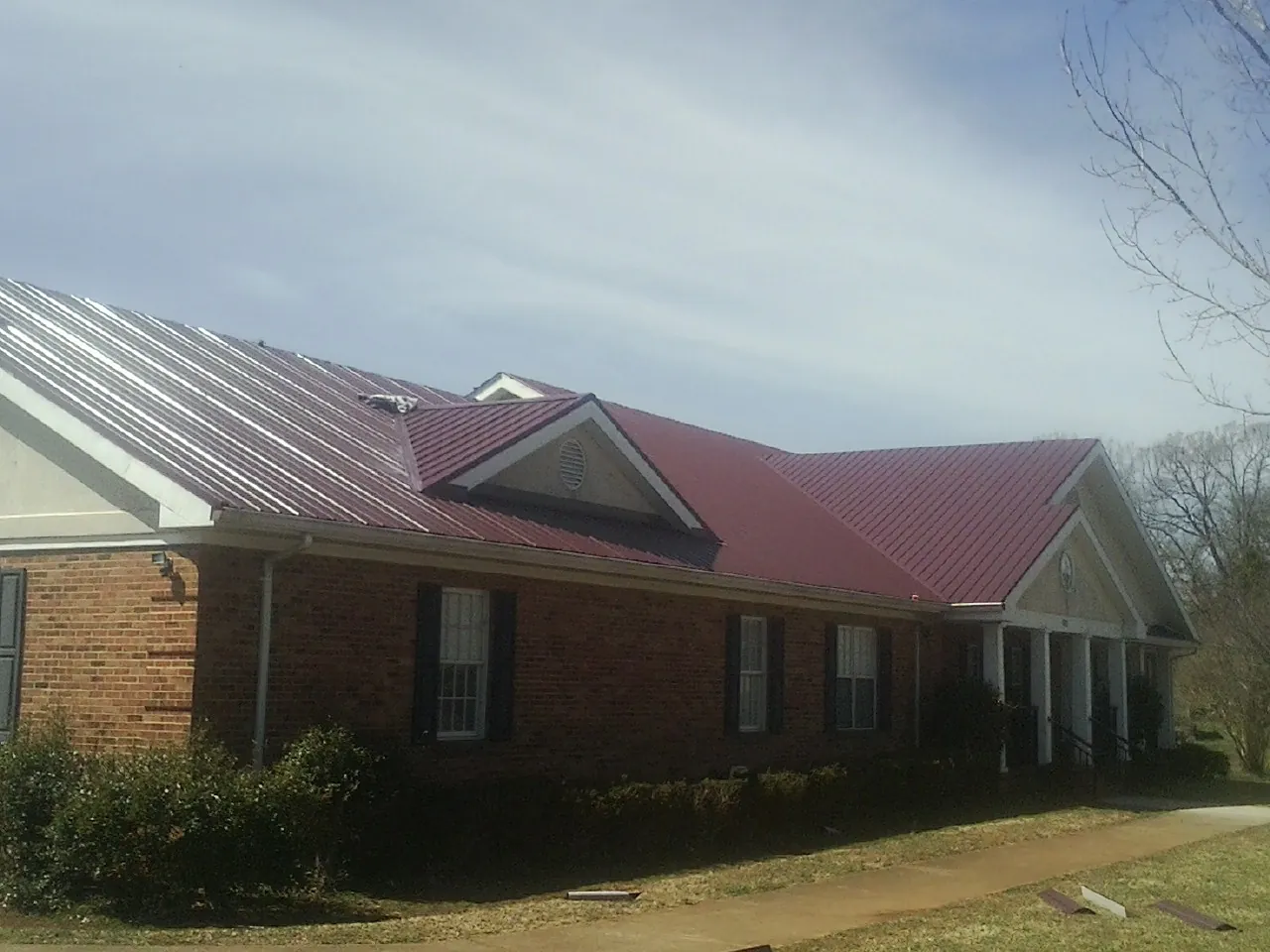 Red metal roof with gabled entries on a long brick building, from a Hail Damage Roof Repair job in Attleboro Falls