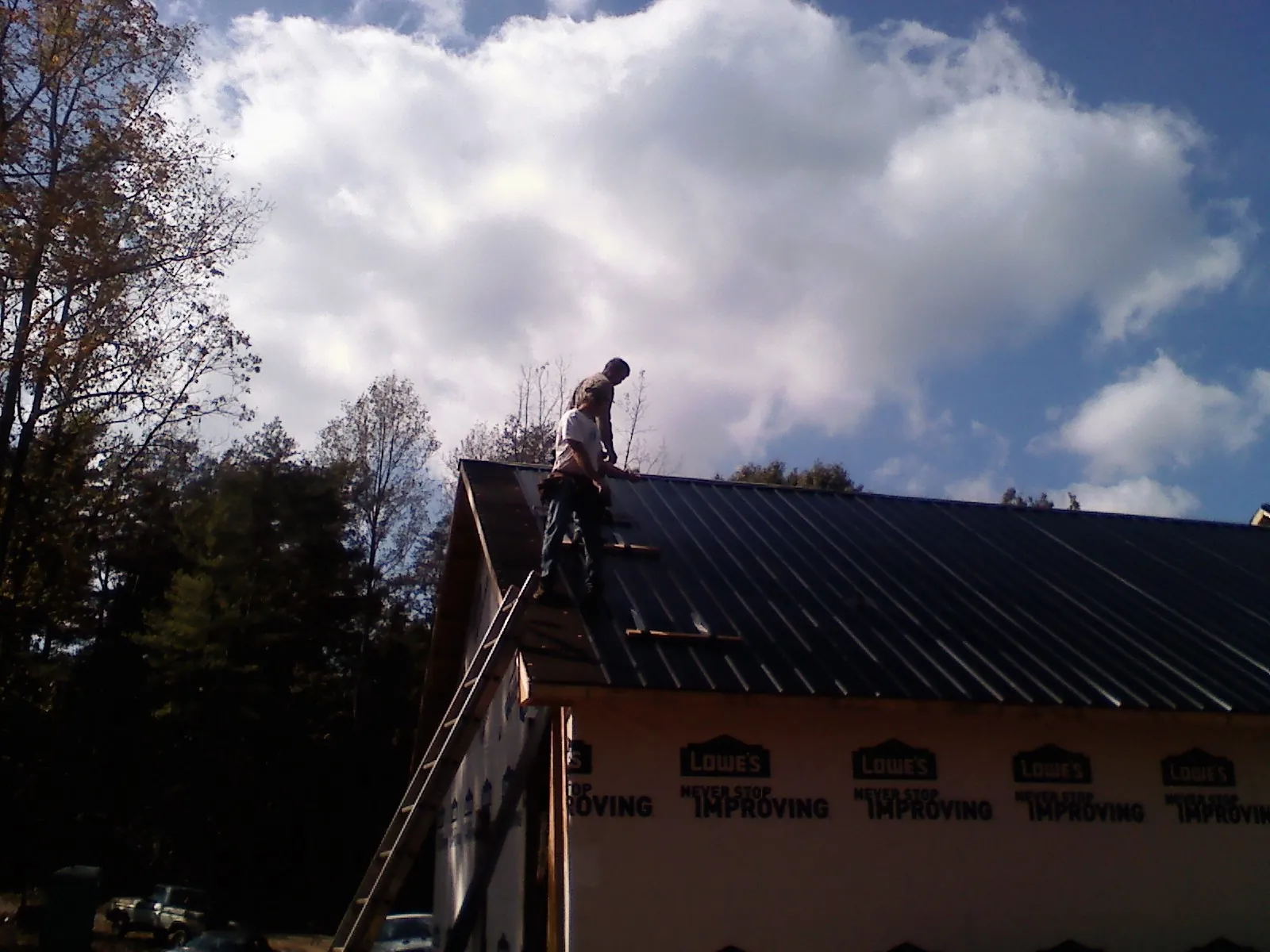 Roofer fastening dark metal panels high against a cloudy sky, from a Roof Inspection job in Attleboro Falls