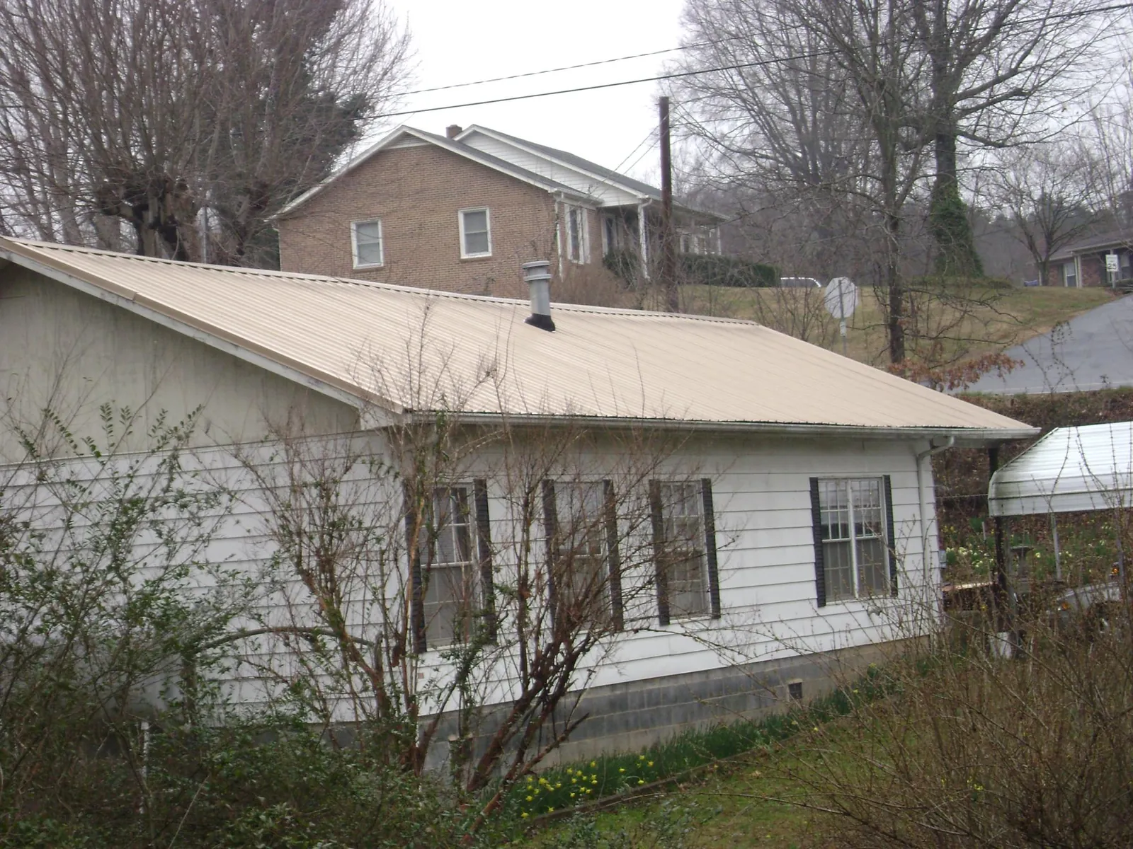 Tan metal roof on a white sided house set into a hillside — Commercial Roofing by Roofing Brothers in Attleboro Falls