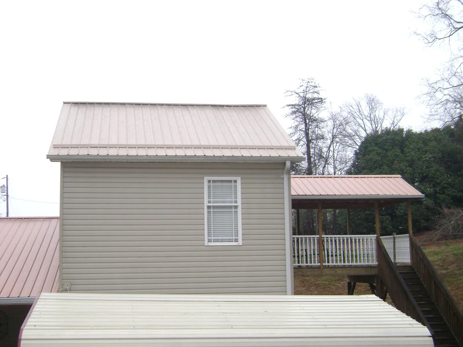 Tan metal roofs on a two story addition and attached porch, from a Roof Replacement job in Attleboro Falls